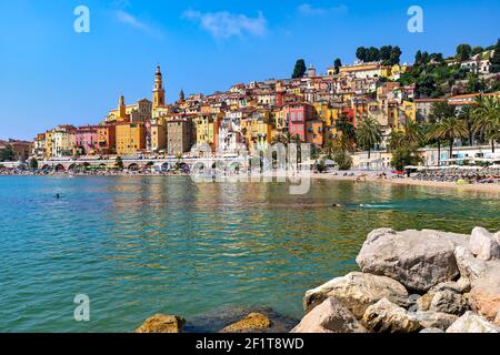 Menschen am Strand entlang der Bucht als bunte Häuser im Hintergrund in Menton - kleine Stadt in Frankreich. Stockfoto