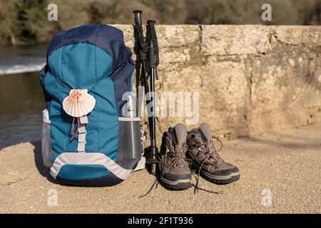 Rucksack mit Muschelsymbol des Camino de Santiago, Trekkingstiefeln und Stöcken, die an einer Steinwand angelehnt sind. Pilgerfahrt nach Santiago de Compostela. Speicherplatz kopieren Stockfoto