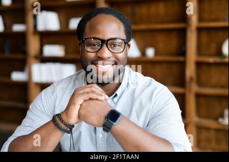 Headshot von freundlichem und selbstbewussten afroamerikanischen Kerl trägt stilvolle Brillen und elegante Freizeitkleidung, schaut auf die Kamera und hält die Hände im Schloss in der Nähe Kinn. Mitarbeiterprofil Stockfoto
