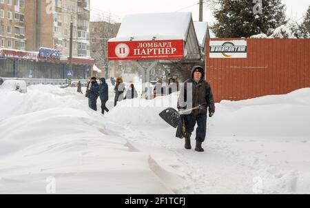 Lutsk, Ukraine - Februar 12,2020: Ein älterer Mann mit Schneeschaufel im Winter. Stadtstraße nach Schneesturm. Die Menschen laufen im Schnee treiben ungereinigt weiter Stockfoto