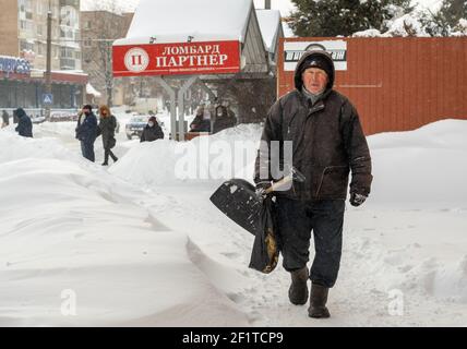 Lutsk, Ukraine - Februar 12,2020: Ein älterer Mann mit Schneeschaufel im Winter. Stadtstraße nach Schneesturm. Die Menschen laufen im Schnee treiben ungereinigt weiter Stockfoto