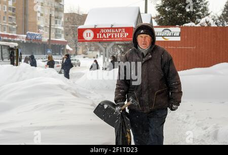 Lutsk, Ukraine - Februar 12,2020: Ein älterer Mann mit Schneeschaufel im Winter. Stadtstraße nach Schneesturm. Die Menschen laufen im Schnee treiben ungereinigt weiter Stockfoto