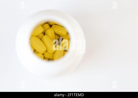 Gelbe lange Vitamine in Pillendose auf weißem Hintergrund, Makro, Nahaufnahme, Kopierraum. Nahrungsergänzungsmittel Konzept, Gesundheit, Vitamine, trendige Farbe