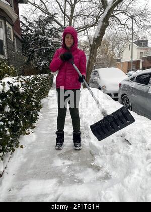 Die junge Frau schaufelt Schnee vom Bürgersteig entlang ihres Hauses im Stadtteil Kensington in Brooklyn, New York. In New York Hausbesitzer sind verantwortlich für die Reinigung von öffentlichen Gehwegen neben ihrem Eigentum. Stockfoto