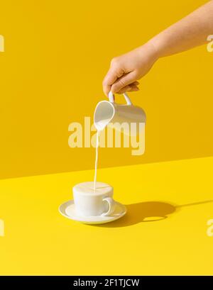 Frau gießt Milch aus einem Krug, in hellem Licht, isoliert auf gelbem Hintergrund. Milch tropft. Frisches Bio-Morgengetränk. Milch übergelaufen. Stockfoto