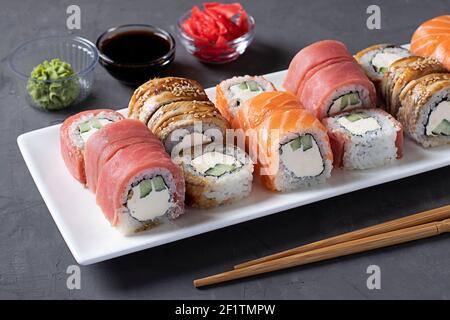 Sushi-Set mit Lachs, Thunfisch und geräuchertem Aal mit philadelphia-Käse auf weißem Teller auf grauem Hintergrund. Serviert mit Sojasauce, Wasabi, eingelegtem Ingwer A Stockfoto