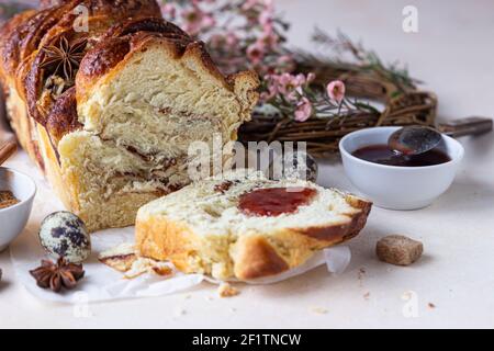 Zimt Babka oder Wirbel Brioche Brot mit Marmelade. Osterhintergrund mit Wachteleiern, Blumen und handgefertigten Kranz aus Zweigen. Zimtbrot. Selektiv Stockfoto