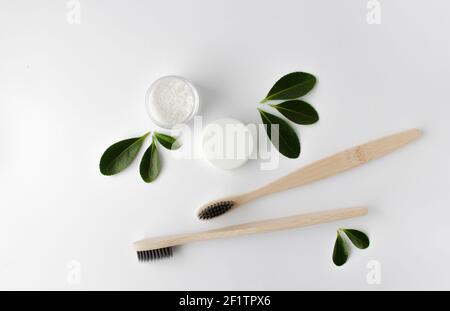 Zwei Holz Bambus umweltfreundliche Zahnbürsten, Gebiss und grüne Blätter auf weißem Hintergrund. Stockfoto