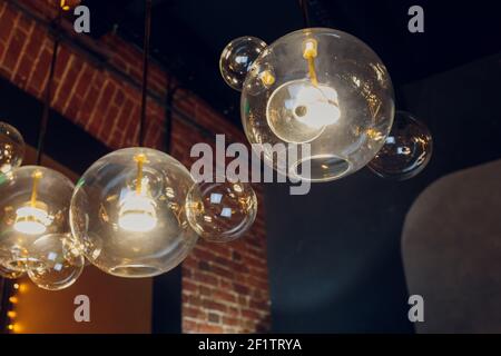 Viele runde Lampen in der Nähe einer braunen Holzwand. Runde Lichter im Innenraum. Hintergrund für Design. Dekorative Glühlampen Stockfoto