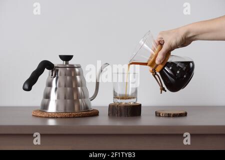 Kaffee in der Hand Tropf Kaffeemaschine zubereiten. Frau Hand gießen Kaffee aus Tropfkaffeemaschine in Glas Vorderansicht Stockfoto