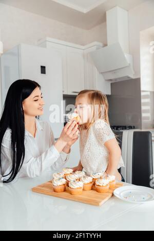 Mutter gibt der Tochter leckere Muffins mit Sahne zu essen Stockfoto