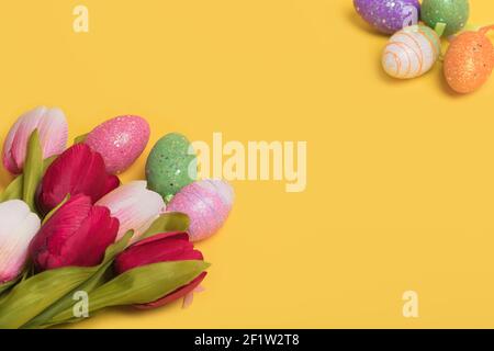 Kreative Osterbordkomposition aus bunten Eiern und Tulpen auf leuchtend gelbem Hintergrund. Minimales osterkonzept. Osterkarte mit Kopie en Stockfoto
