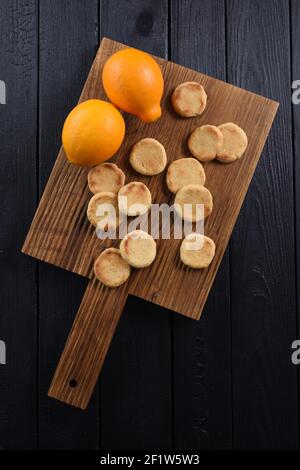 Eichenbrett mit hausgemachten Plätzchen und Bio-Zitronen auf schwarz Hintergrund über Ansicht von oben Stockfoto