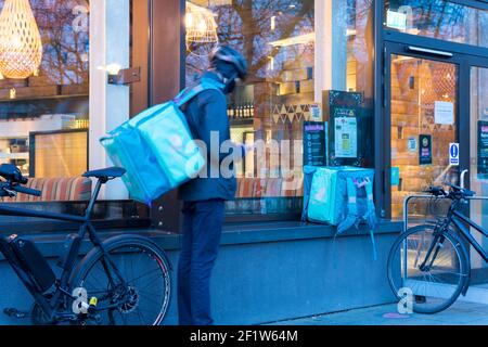 Deliveroo Rider steht und überprüft sein Telefon auf Bereitschaft seiner Abholbestellung außerhalb des Restaurants, London greenwich Stockfoto