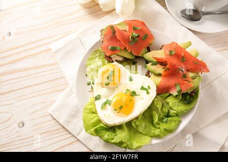 Zwei Spiegeleier in Herzform, Sandwiches mit Avocado und geräuchertem Lachs auf Salat, Rezept mit Liebe zum osterfest oder Valentinstag, weiß aus Holz Stockfoto