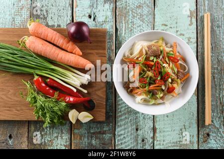 Gesunde Ernährung. Traditionelle asiatische udon-Nudeln und Rohstoffe: Zwiebel, Karotte, Frühlingszwiebeln, Chili und Knoblauch auf rustikalem blauen Hintergrund Draufsicht Stockfoto