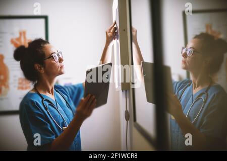 Seitenansicht einer lächelnden Krankenschwester mittleren Alters, die die Röntgenaufnahme in einer Arztpraxis überprüft. Stockfoto