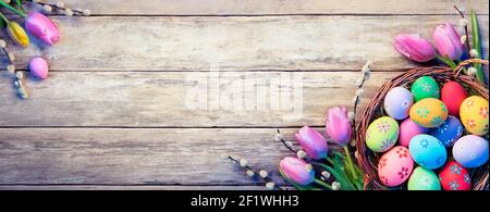 Osterdekoration - Painted Eggs In Basket With Tulpen On Natürliche Holzplanke Stockfoto