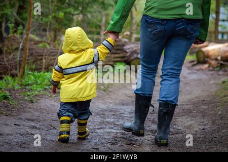 Mutter und Kleinkind gehen für einen Spaziergang auf einem schlammigen Trail trägt Stiefel und Regenmäntel Stockfoto