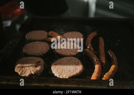 Eine Draufsicht auf neue hinzugefügte Würste und Koteletts Ein öliger Brazier in der Küche unter den Sonnenstrahlen Stockfoto