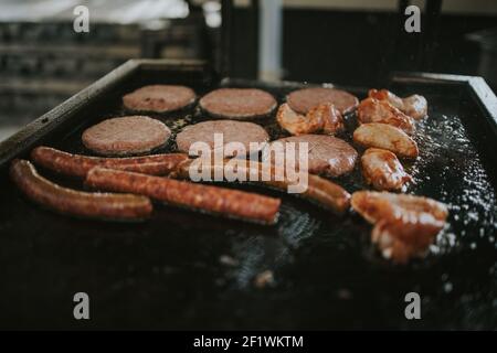 Eine Seitenansicht von neu hinzugefügten Würstchen und Koteletten Ein öliger Brazier in der Küche mit Ölspritzern Stockfoto
