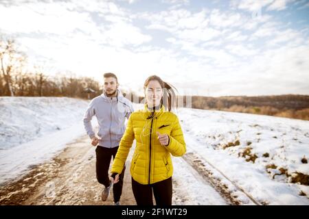 Zwei sportlich fröhliche Fitnessfreunde laufen an einem Wintertag in der schneebedeckten Natur. Stockfoto