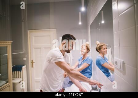 Charmantes, reizend lächelndes Paar im Schlafanzug, das vor dem Spiegel im Badezimmer ein Gespräch führt. Stockfoto