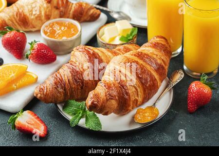 Frische süße Croissants mit Butter und Orangenmarmelade zum Frühstück. Kontinentales Frühstück auf einem schwarzen Betontisch. Stockfoto