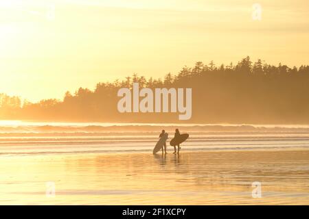 Zwei Surfer am Strand bei Sonnenuntergang. Stockfoto