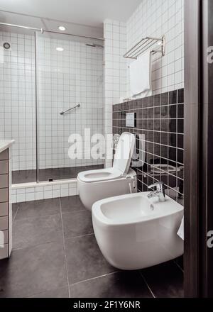 Modernes Badezimmer mit Toilette kombiniert. Dusche und WC sind mit weißen und schwarzen Fliesen schwarzen Boden bedeckt Stockfoto
