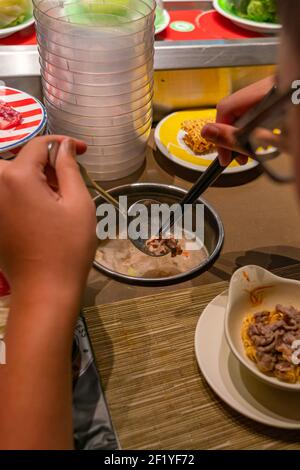 Nahaufnahme Foto von Frau mit Essstäbchen und Essen an Hotpot-Restaurant für Förderband Stockfoto