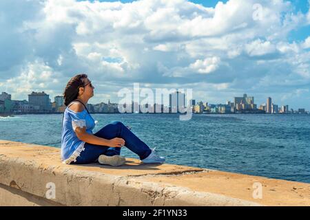 Frau, die auf der Malecon in Havanna vor dem Meer sitzt. Stockfoto