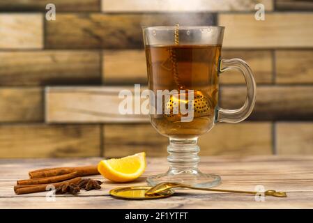Vintage Tee Sieb und Glas Tee auf einem Holztisch mit Zitrone und Zimt. Goldenes Teekanne-Sieb. Stockfoto