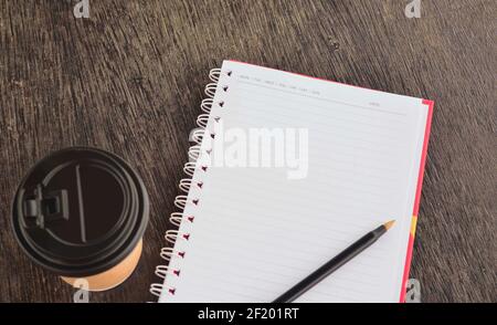Notizblock mit Einweg-Kaffeetasse und Stift auf Holztisch Stockfoto