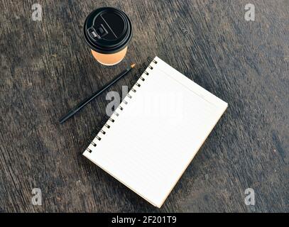 Notizblock mit Einweg-Kaffeetasse und Stift auf Holztisch Stockfoto