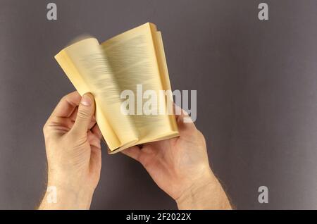 Verschwommene Bewegung der Hand Umdrehen Seite über grauen Hintergrund. Männliche Hände blättern schnell durch ein altes Buch mit vergilbten Seiten. Mann mittleren Alters, kaukasisch. Stockfoto