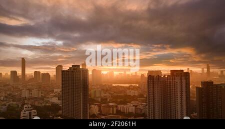 Stadtbild mit Wolkenkratzer und Morgensonne. Stadt am Fluss mit orangefarbenem Sonnenaufgang. Urbanes modernes Gebäude. Überfüllt mit Apartmentgebäude. Stockfoto