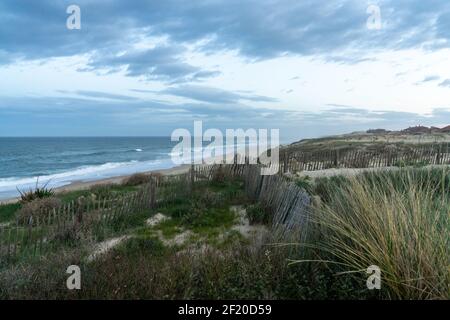 Sanddünen und Wellen brechen an einem endlosen Strand unter Ein stürmischer Himmel in Frankreich Stockfoto