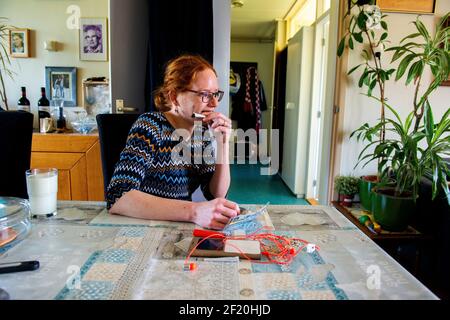 Roosendaal, Niederlande. Junge Erwachsene rothaarige Frau, die mit Tabak eine Zigarette raucht, während sie an ihrem häuslichen Esstisch sitzt. Stockfoto