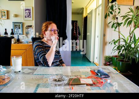 Roosendaal, Niederlande. Junge Erwachsene rothaarige Frau, die mit Tabak eine Zigarette raucht, während sie an ihrem häuslichen Esstisch sitzt. Stockfoto