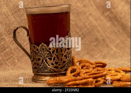 Gesalzene Brotstangen und gesalzene Brezeln in loser Schüttung und ein Glas Tee in einem Getränkehalter auf dem Tisch. Nahaufnahme mit selektivem Fokus. Stockfoto