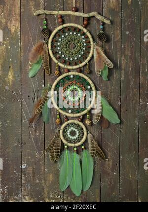 Schöner handgefertigter Boho-Traumfänger mit grünen Federn und Perlen. Mystischer Hintergrund mit Traumfänger gegen Holzbretter, esoterisch, ethnisch und s Stockfoto