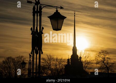 Silhouette der Peter-und-Paul-Kathedrale bei Sonnenuntergang und die alte Laterne mit einem Pfeil (St. Petersburg, Russland) Stockfoto