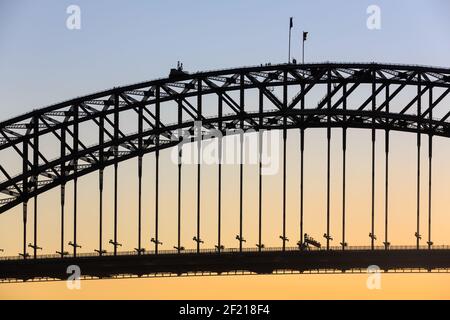 Ein Teil der Sydney Harbour Bridge wurde vor dem Sonnenuntergang in den Himmel geschildet. Eine Gruppe von Brückenkletterern ist nur an der Spitze sichtbar Stockfoto