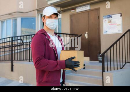 Kurier in medizinischen Gummihandschuhe und Schutzmaske hält Kartons. Türzustellung. Essen zum Mitnehmen. Lieferservice. Quarantäne. Coronavirus. Stockfoto