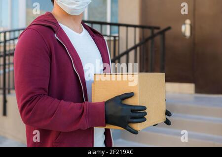Kurier in medizinischen Gummihandschuhe und Schutzmaske hält Kartons. Türzustellung. Essen zum Mitnehmen. Lieferservice. Quarantäne. Coronavirus. Stockfoto