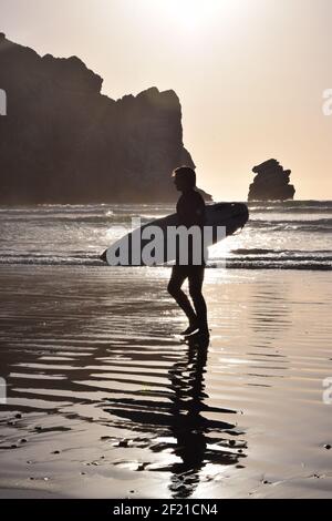 FRESNO, USA - Mär 04, 2021: Ein Foto aus nächster Nähe einer Silhouette eines männlichen Surfers, der sein Surfboard gegen eine weiche, glühende Sonne hält, die sein R zeigt Stockfoto