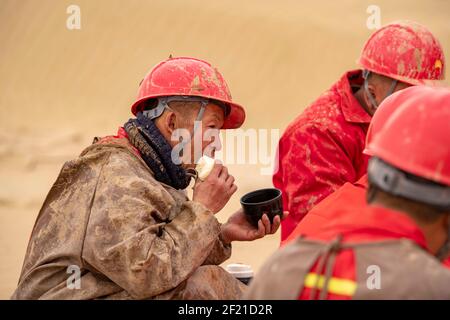 (210310) --URUMQI, 10. März 2021 (Xinhua) -- Arbeiter des geophysikalischen Vermessungsteams essen am 25. Februar 2021 in der Taklimakan-Wüste im Nordwesten Chinas, der Autonomen Region Xinjiang Uygur. Die Taklimakan-Wüste im Tarim-Becken der Autonomen Region Xinjiang Uygur im Nordwesten Chinas ist eine der größten petroliferösen Regionen Chinas und aufgrund ihrer rauen Bodenbedingungen und der komplizierten unterirdischen Bedingungen eine der schwierigsten zu erkunden. Die Erkundung der Öl- und Gasressourcen erfordert mehrere Prozesse, einschließlich der Durchführung geophysikalischer Untersuchungen, um seismische Daten zu sammeln, um eine Soli zu legen Stockfoto