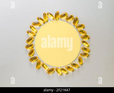 Vitamin D3 flüssige Kapseln um gelben Kreis auf neutralem grauen Hintergrund. Draufsicht oder flach legen gelbe Sonne mit Papier Kreis und flüssige Kapseln mit Kopierraum gemacht. Stockfoto