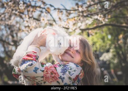 Liebenswert schöne Mädchen mit langen blonden Haaren umarmt weißen Ostern Kaninchentier Stockfoto